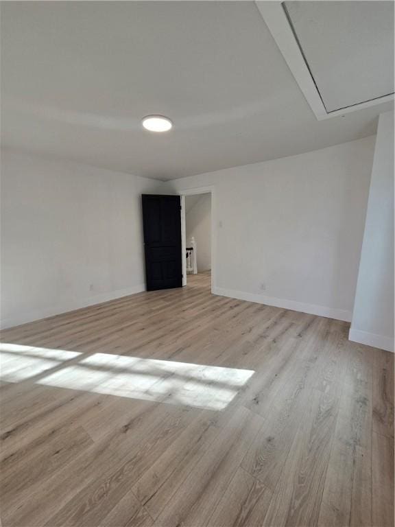 unfurnished room featuring light wood finished floors, attic access, and baseboards