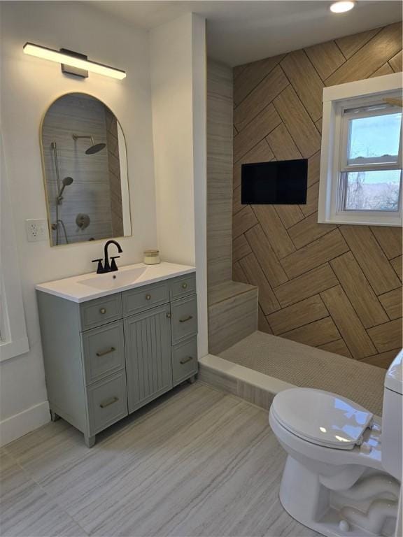 bathroom with toilet, a tile shower, vanity, and baseboards