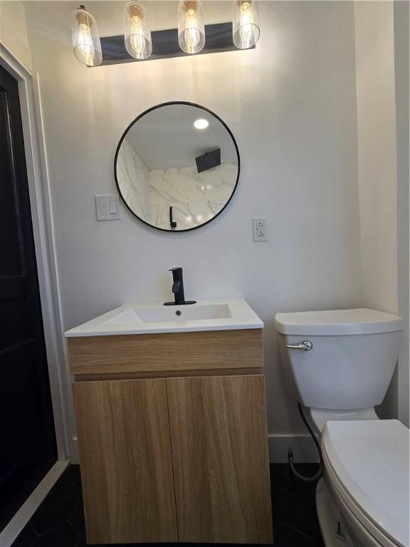 half bath with toilet, baseboards, vanity, and tile patterned floors