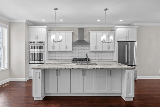 kitchen featuring a kitchen island with sink, a sink, white cabinetry, wall chimney range hood, and appliances with stainless steel finishes