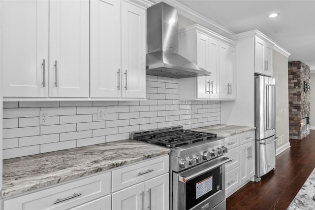 kitchen with dark wood-style floors, high end appliances, tasteful backsplash, white cabinets, and wall chimney range hood