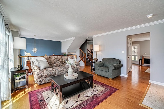 living area with baseboards, stairway, wood finished floors, crown molding, and a textured ceiling