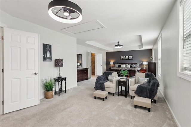 living area with carpet, a raised ceiling, attic access, and baseboards