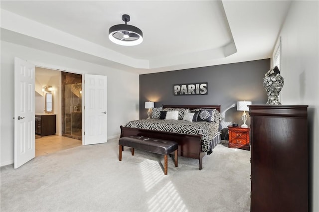 carpeted bedroom with baseboards, a tray ceiling, and ensuite bathroom