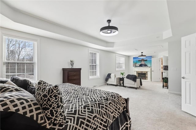 carpeted bedroom with multiple windows, a fireplace, and a raised ceiling