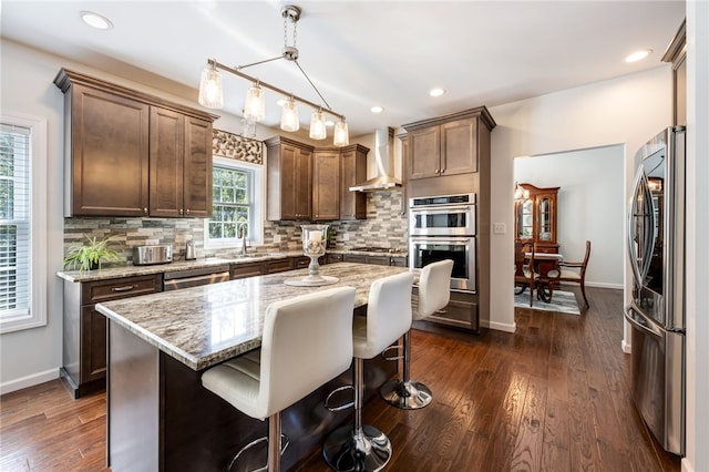 kitchen featuring wall chimney range hood, decorative backsplash, stainless steel appliances, and a sink