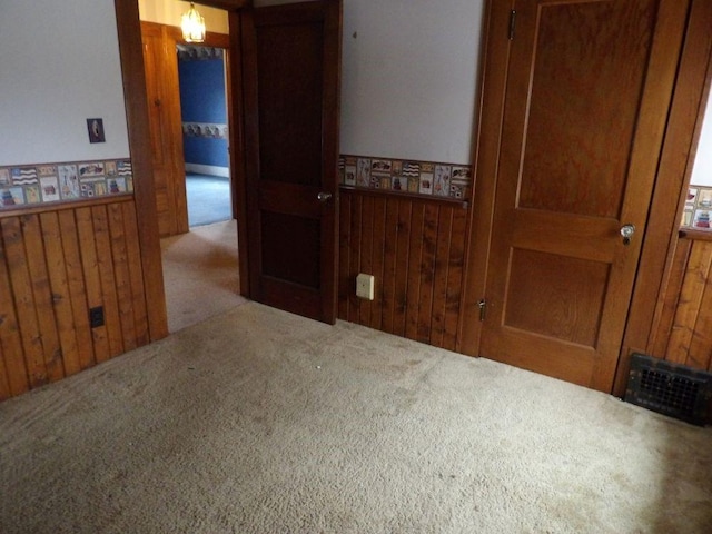 carpeted empty room featuring wood walls, wainscoting, and visible vents