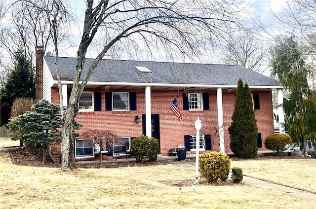 split foyer home featuring roof with shingles, brick siding, and a chimney