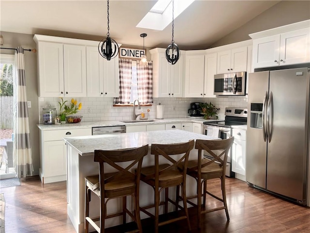 kitchen with vaulted ceiling with skylight, dark wood-type flooring, a kitchen island, a sink, and appliances with stainless steel finishes