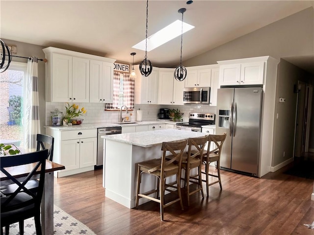 kitchen with a center island, appliances with stainless steel finishes, white cabinetry, vaulted ceiling, and a sink