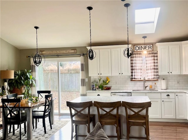 kitchen with a sink, white cabinets, hanging light fixtures, stainless steel dishwasher, and backsplash