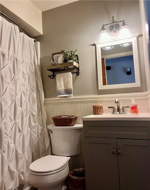 bathroom featuring a wainscoted wall, vanity, toilet, and a shower with curtain