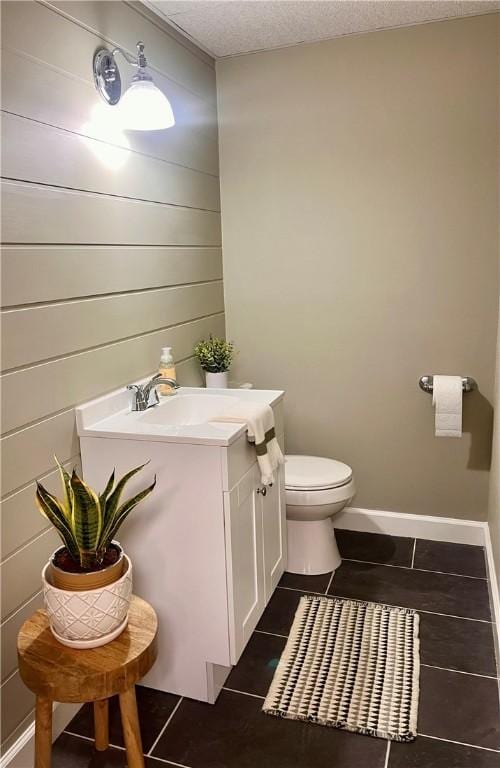 half bathroom featuring toilet, baseboards, a textured ceiling, and vanity