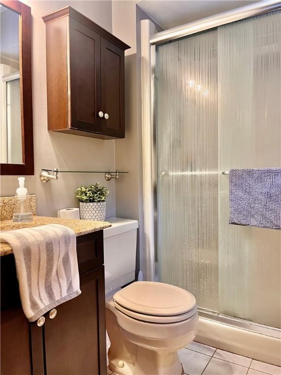 full bath with toilet, a stall shower, vanity, and tile patterned floors