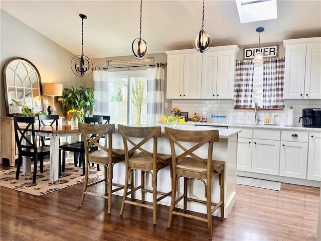 kitchen with lofted ceiling, a kitchen island, dark wood-type flooring, white cabinetry, and backsplash