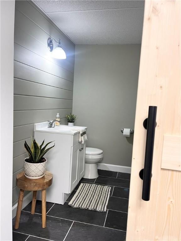 half bathroom featuring baseboards, toilet, tile patterned floors, a textured ceiling, and vanity