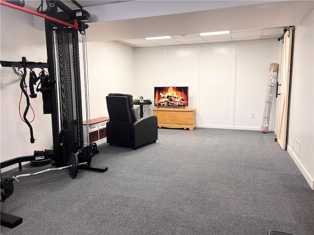 exercise area with a warm lit fireplace, carpet flooring, and a paneled ceiling