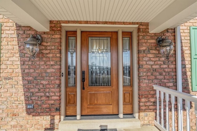 doorway to property featuring a porch and brick siding