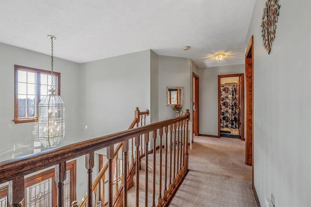 corridor featuring light colored carpet, a textured ceiling, an upstairs landing, a chandelier, and baseboards