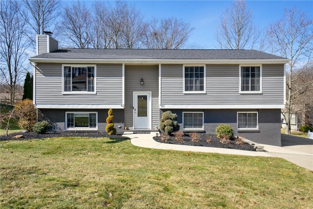 bi-level home with concrete driveway, brick siding, a chimney, and a front lawn