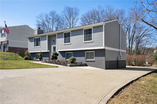 raised ranch featuring driveway, a chimney, a front lawn, and brick siding