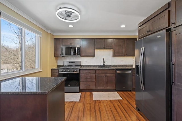 kitchen featuring stainless steel appliances, wood finished floors, a sink, dark brown cabinets, and dark stone counters