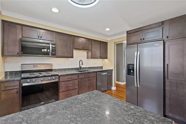 kitchen with stainless steel appliances, wood finished floors, a sink, backsplash, and dark stone countertops