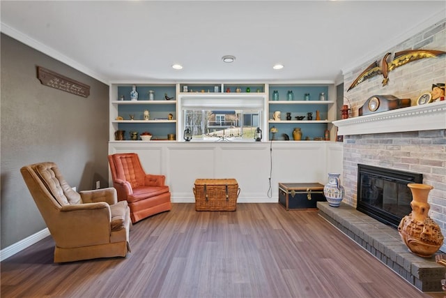 living area with crown molding, a fireplace, baseboards, and wood finished floors