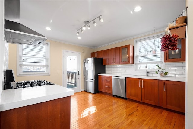 kitchen featuring wall chimney exhaust hood, appliances with stainless steel finishes, a sink, and brown cabinets