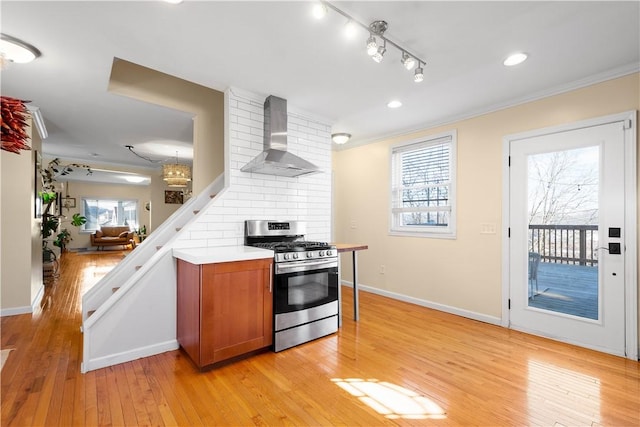 kitchen with stainless steel range with gas cooktop, crown molding, brown cabinetry, light wood-style floors, and wall chimney exhaust hood