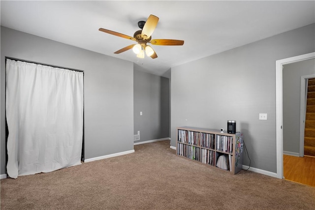 carpeted empty room with a ceiling fan, stairway, and baseboards