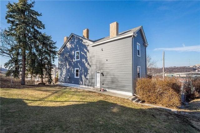 back of house featuring a patio area, a lawn, and a chimney