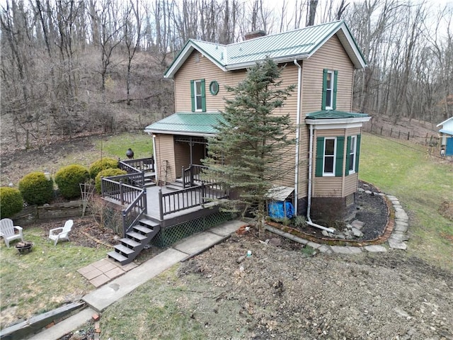 view of front facade with a chimney, an outdoor fire pit, metal roof, a deck, and a front lawn