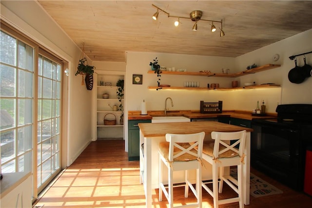 kitchen featuring black range with electric cooktop, butcher block countertops, a sink, a wealth of natural light, and open shelves