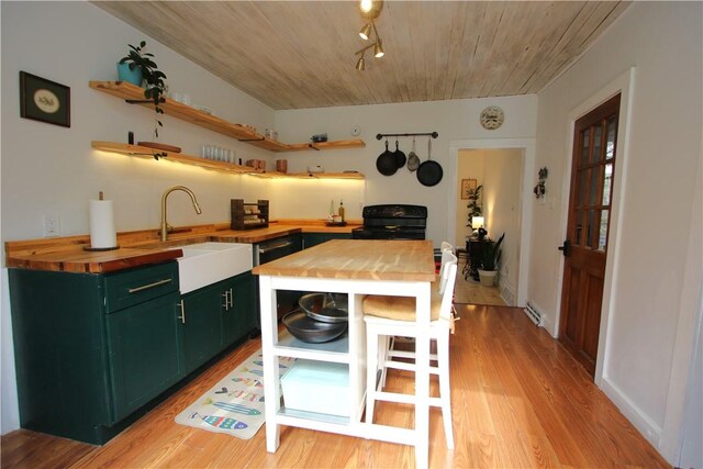 kitchen featuring light wood finished floors, open shelves, green cabinets, a sink, and butcher block countertops