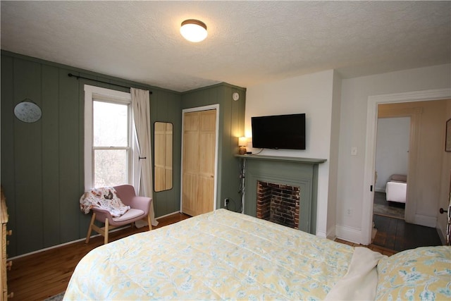 bedroom with a textured ceiling, a fireplace, baseboards, a closet, and dark wood-style floors