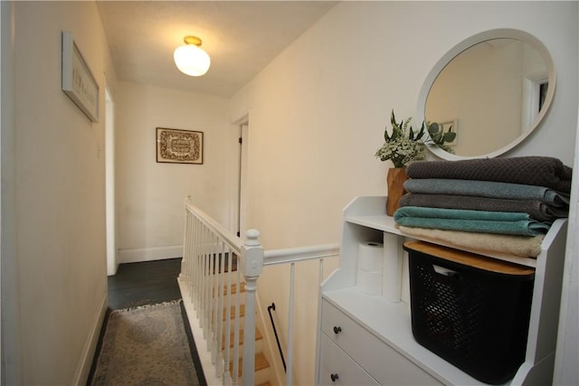 hall with dark wood-type flooring, an upstairs landing, and baseboards