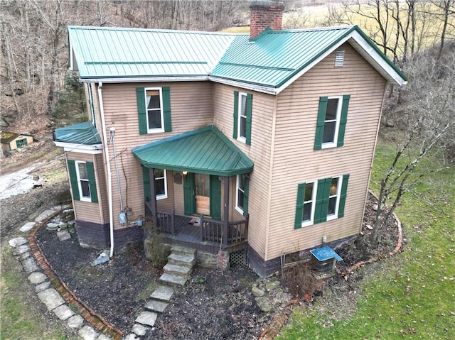 view of front of house with metal roof, a standing seam roof, a chimney, and a porch