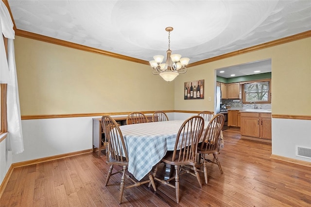 dining space featuring light wood-type flooring, crown molding, and a notable chandelier