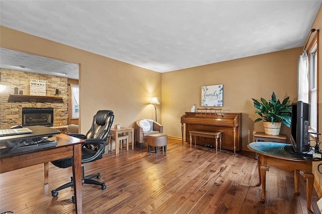 home office featuring a stone fireplace, wood-type flooring, and baseboards