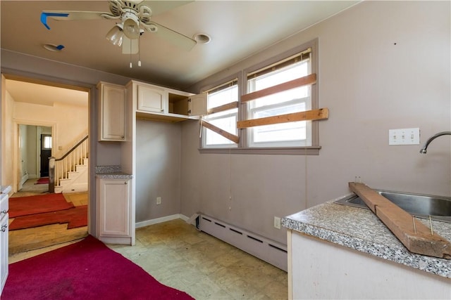 interior space with a ceiling fan, baseboard heating, light countertops, light floors, and a sink