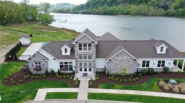 view of front of property with a front yard, stone siding, a water view, and a wooded view