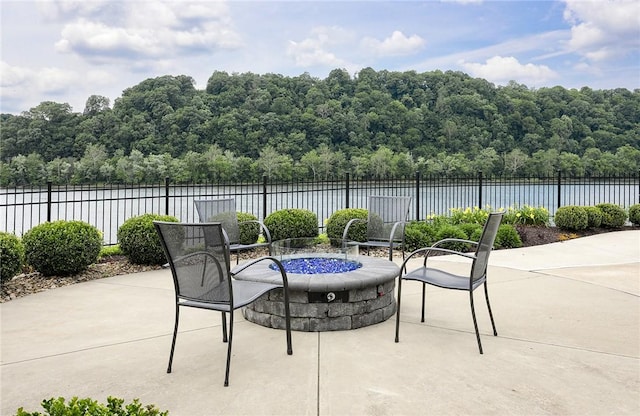 view of patio featuring an outdoor fire pit, a view of trees, a water view, and fence