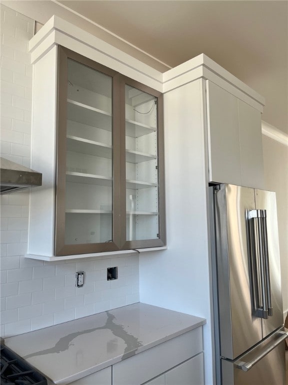 kitchen featuring freestanding refrigerator, tasteful backsplash, white cabinetry, and light stone counters