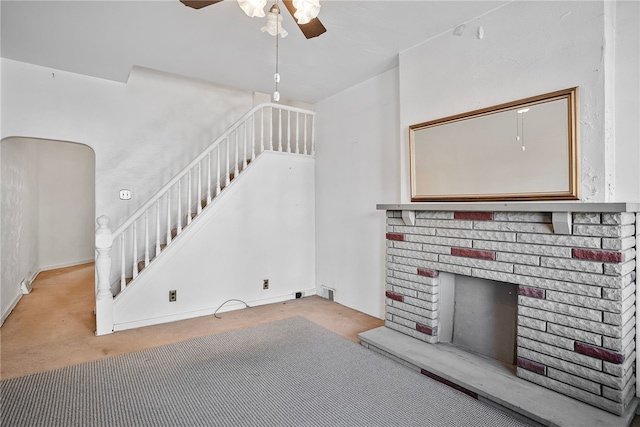 unfurnished living room featuring a ceiling fan, carpet, a brick fireplace, and stairs