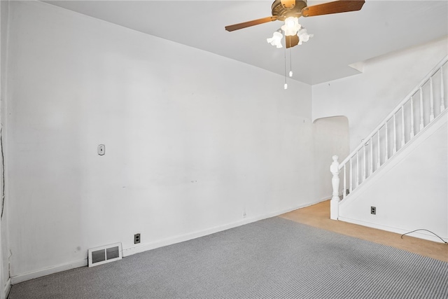 carpeted empty room featuring baseboards, visible vents, arched walkways, a ceiling fan, and stairs