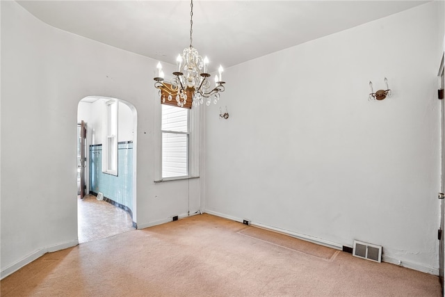 spare room featuring light carpet, visible vents, arched walkways, and a chandelier