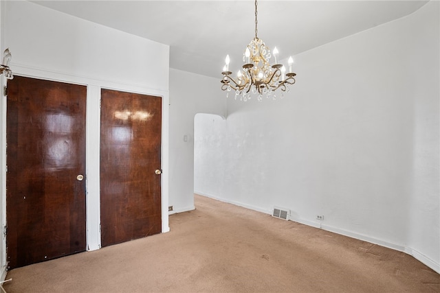 carpeted empty room with visible vents, baseboards, and an inviting chandelier