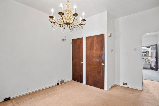 unfurnished bedroom featuring visible vents, arched walkways, carpet, multiple closets, and a notable chandelier