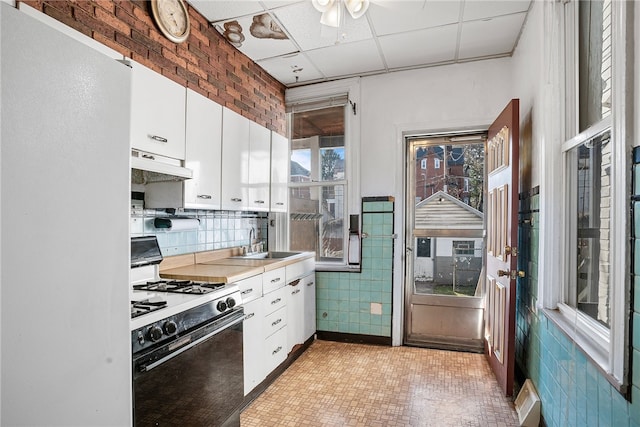 kitchen featuring under cabinet range hood, a sink, white cabinetry, and range with gas stovetop